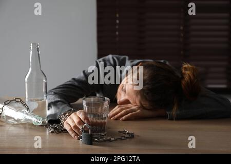 Dépendance à l'alcool. Femme enchaînée avec un verre de vodka dormant sur une table en bois dans la chambre Banque D'Images