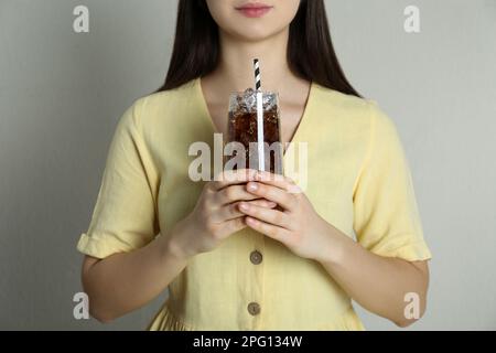 Femme tenant un verre de cola avec de la glace et de la paille sur fond beige, gros plan. Soda rafraîchissante Banque D'Images