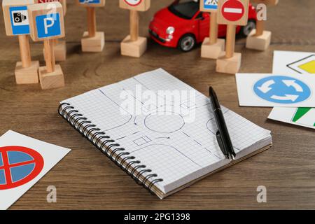 Nombreux panneaux de signalisation, carnet avec croquis de rond-point et voiture jouet sur table en bois. École de conduite Banque D'Images