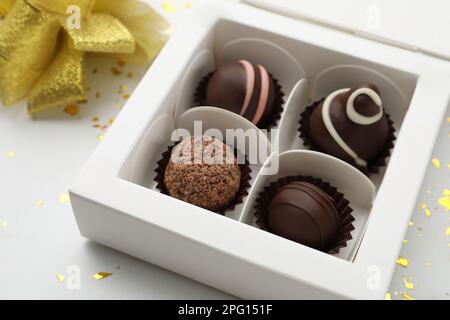 Différents délicieux truffes au chocolat en boîte, noeud et confetti sur fond blanc, gros plan Banque D'Images