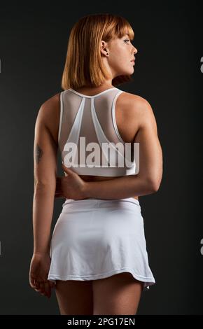 Ne vous laissez pas duper par cet adorable ensemble. Vue arrière d'une femme portant des vêtements de sport sur un fond sombre. Banque D'Images