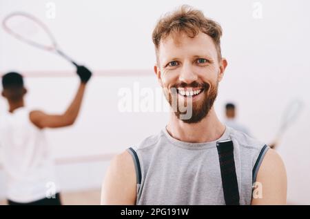 Rejoignez-nous pour une partie de squash. Portrait d'un jeune homme jouant un match de squash avec ses coéquipiers en arrière-plan. Banque D'Images