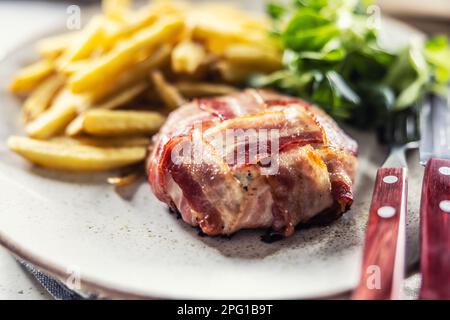 Fromage camambert enveloppé de tranches de bacon et poêlé, servi avec des frites et de la salade verte. Banque D'Images