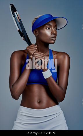 Je suis prêt pour tout ce que la vie me lance. Photo studio d'une jeune femme sportive posant avec une raquette de tennis sur fond gris. Banque D'Images