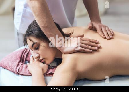 Le masseur fait un massage relaxant des muscles du trapezius et de retour au client allongé sur le canapé Banque D'Images