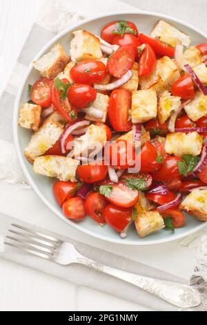 Salade d'été délicieuse de tomates cerises, pain rassis, oignon, huile d'olive et jus de tomate dans une assiette sur la table. Vue verticale du dessus de abo Banque D'Images