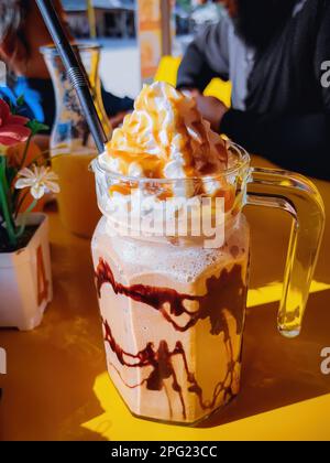Frappuccino dans une grande tasse de verre sur la table au café par temps ensoleillé. Banque D'Images