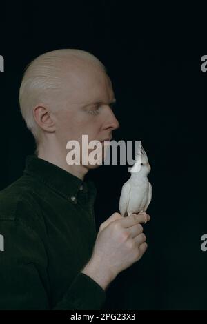 Un type albino avec un perroquet blanc sur un fond sombre Banque D'Images