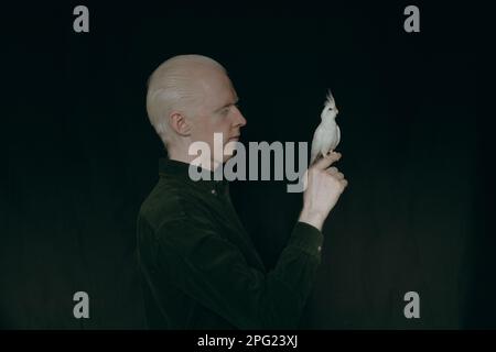 Un type albino avec un perroquet blanc sur un fond sombre Banque D'Images