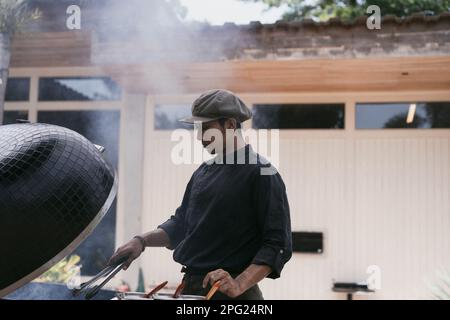 Homme asiatique en uniforme cuisiniers sur le grill à l'extérieur. Personnel de cuisine, Banque D'Images