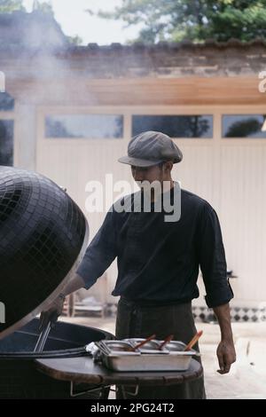 Homme asiatique en uniforme cuisiniers sur le grill à l'extérieur. Personnel de cuisine, Banque D'Images