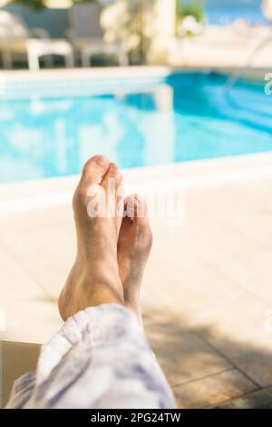 Mâle pieds nus touristes se détendre au bord de la piscine extérieure dans la station balnéaire le jour ensoleillé d'été, pov tourné avec un foyer sélectif Banque D'Images