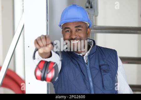 un travailleur masculin tenant une paire de casque antibruit vers l'avant Banque D'Images