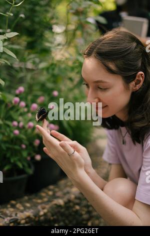 Jeune femme tenant un papillon dans ses mains et souriant Banque D'Images