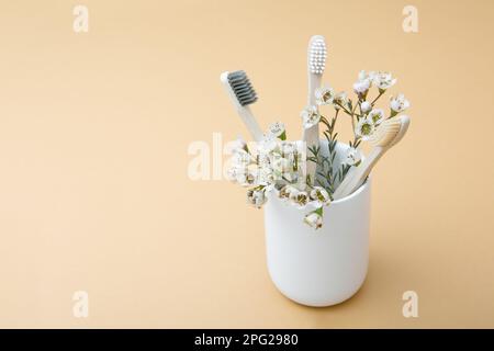 Brosses à dents et fleurs en bambou en bois dans un verre blanc sur fond beige. Le concept de durabilité et le rejet du plastique. Le concept Banque D'Images