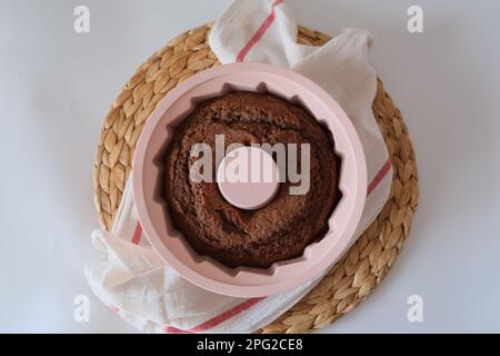 Gâteau cuit dans un moule, il y a un gâteau caçao cuit dans un moule en silicone rond rose sur un tissu blanc de cuisine et un napperon sur la table de cuisine. Banque D'Images