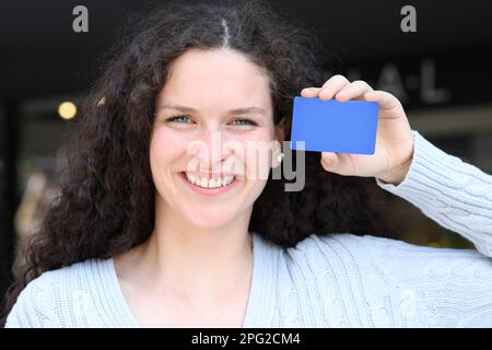 Vue avant portrait d'une femme montrant une carte de crédit bleue vierge dans la rue Banque D'Images