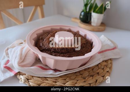 Gâteau cuit dans un moule, gâteau cuit dans un moule en silicone rond rose sur un tissu blanc de cuisine et un napperon sur la table de cuisine. La photo de concept. Banque D'Images