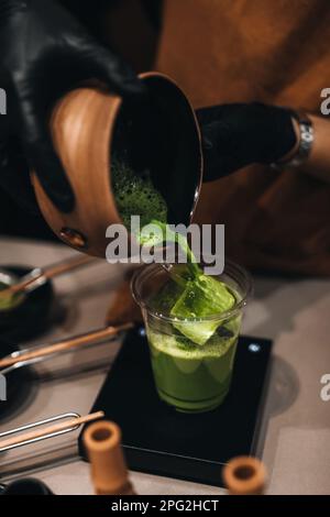 Processus de préparation du thé vert japonais Matcha. Les mains des femmes versent du matcha dans un verre en plastique. Ustensiles biologiques traditionnels. Banque D'Images
