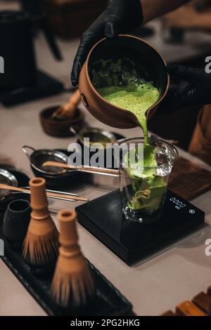 Processus de préparation du thé vert japonais Matcha. Les mains des femmes versent du matcha dans un verre en plastique. Ustensiles biologiques traditionnels. Banque D'Images