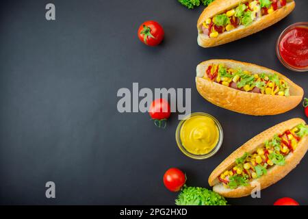 Hot dog avec des cornichons, des tomates et de la laitue sur un fond sombre. Restauration rapide. Calorie alimentaire. Vue de dessus. Espace pour la copie. Banque D'Images
