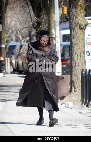 Un juif hassidique dans un long manteau avec de hauts bas noirs marche sur Bedford Avenue sur un hiver froid par exemple. Les mains à l'intérieur des manches sont une pose familière. Banque D'Images