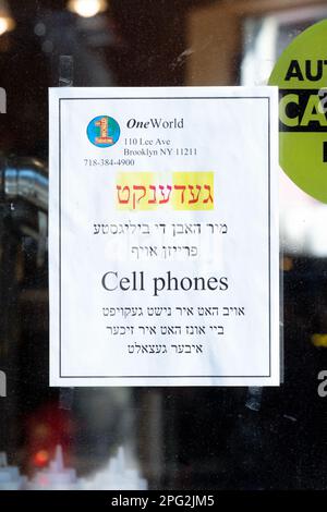 Un panneau bilingue dans une fenêtre de boulangerie annonçant pour les téléphones cellulaires à bas prix. À Williamsburg, Brooklyn, New York. Banque D'Images