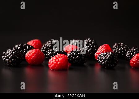 Une poignée de framboises et de mûres sur fond noir. Fruits sains sur fond sombre avec gouttes d'eau Banque D'Images