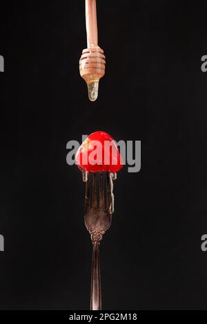 La moitié d'une fraise sur une fourchette ancienne sur un fond sombre gros plan. Le miel coule sur les fraises. Banque D'Images