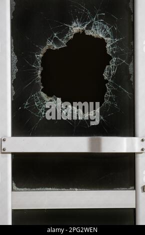un trou de balle en verre est un trou de balle réel d'une balle de projectile de grand calibre. Porte vitrée percée d'une balle pendant la guerre, attaque terroriste. BR Banque D'Images