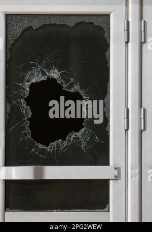 un trou de balle en verre est un trou de balle réel d'une balle de projectile de grand calibre. Porte vitrée percée d'une balle pendant la guerre, attaque terroriste. BR Banque D'Images