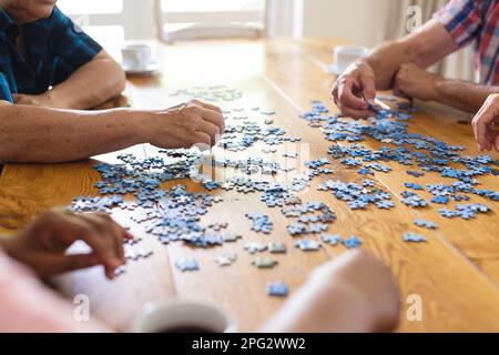 Les mains de divers amis âgés assis à table faisant le puzzle ensemble Banque D'Images