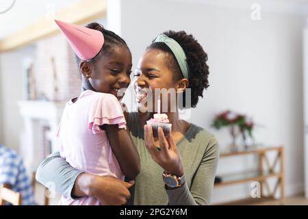 Bonne mère et fille afro-américaine célébrant l'anniversaire, tenant un cupcake avec une bougie Banque D'Images