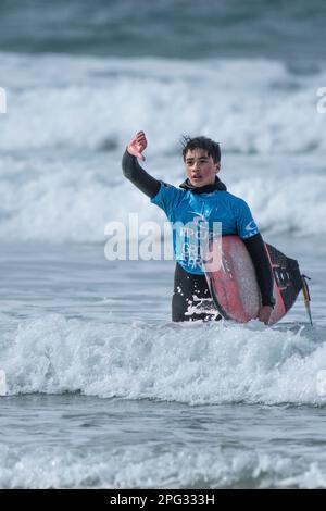 Un jeune surfeur mâle portant son surf en bas de pouce et marchant hors de la mer après avoir conté dans le RIP Curl Grom Search Surfing concurrente Banque D'Images