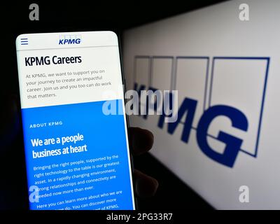Personne tenant un téléphone portable avec la page Web de la société de services professionnels KPMG à l'écran devant le logo. Concentrez-vous sur le centre de l'écran du téléphone. Banque D'Images