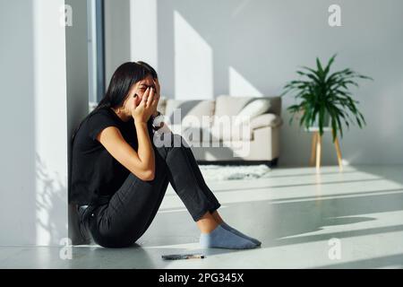 Jeune femme en vêtements décontractés qui pleure seule à la maison pendant la journée Banque D'Images