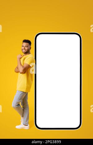 Charmant Indien 20s Indien gars debout près d'un immense smartphone avec écran vide vide et le doigt de pointage, la publicité nouvelle application mobile, meilleure affaire ou promotion, maquette, espace de copie Banque D'Images