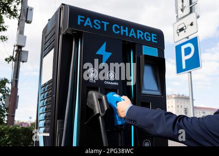 un homme d'affaires facture une voiture électrique. une station de charge de la batterie de voiture électrique dans une rue de ville. Une station-service moderne avec électricité. Banque D'Images