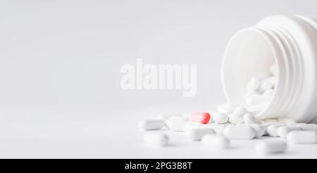 Des pilules blanches avec un rouge ont été déversées d'un pot en plastique. Capsules de médicaments sur fond blanc avec espace de copie. Banque D'Images