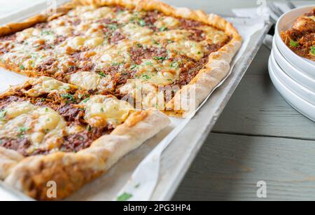 Pizza carrée avec bœuf haché, fromage, tomates, poivrons, oignons et herbes sur une plaque à pâtisserie Banque D'Images