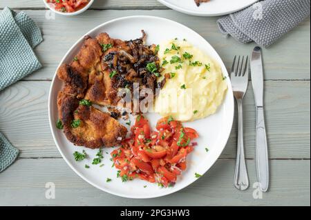 Assiette de schnitzel de porc pané, oignons frits, purée de pommes de terre et salade de tomates Banque D'Images