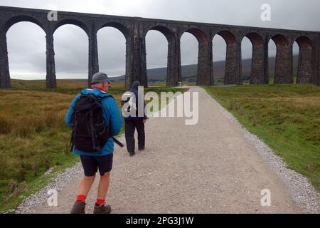 Deux hommes (randonneurs) marchant sur une piste jusqu'au viaduc de chemin de fer de Stone Ribblehead dans le parc national de Yorkshire Dales, Yorkshire, Angleterre, Royaume-Uni. Banque D'Images