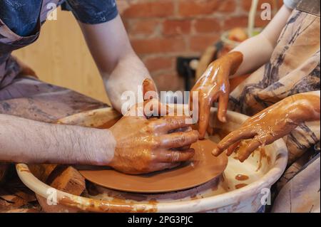 potter enseigne l'enfant. Un artisan est assis sur un banc avec une roue de potier et fait un pot en argile. Artisanat national. Gros plan des mains. Banque D'Images