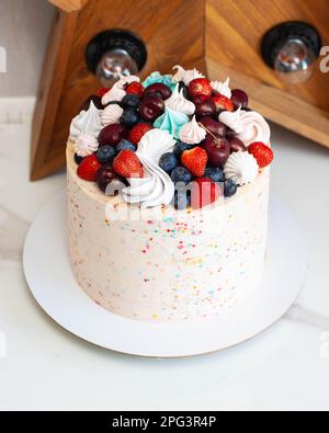Joyeux gâteau d'anniversaire avec des saupoudriers, des cerises, des fraises, des bleuets et des meringues Banque D'Images