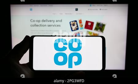 Personne tenant un smartphone avec le logo de la société de détail Co-operative Group Limited à l'écran devant le site Web. Mise au point sur l'affichage du téléphone. Banque D'Images