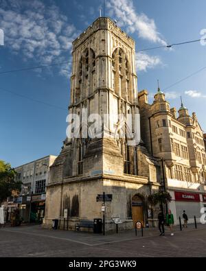 Des piétons marchent le long de la tour de l'église St Michael's dans le quartier commerçant Eastgate du centre-ville de Gloucester. Banque D'Images