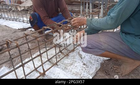 Les mains de l'ouvrier qui tracent des tiges de fer avec du fil pour la section de poutre sur le chantier de construction Banque D'Images