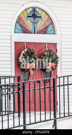 Porte rouge de l'église luthérienne de l'espoir avec deux couronnes de Noël et une fenêtre en arc-en-ciel avec une croix le jour d'hiver à Toivola, Minnesota, États-Unis. Banque D'Images