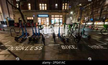 Les scooters électriques et les vélos de location sans quai sont alignés dans une aire de stationnement marquée pour tenter de réduire l'encombrement des trottoirs à Bloomsbury, dans le centre de Londres. Banque D'Images