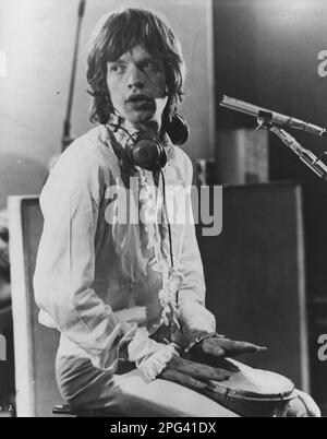 Le rocker britannique, Mick Jagger, chanteur principal des Rolling Stones, assis dans le studio sur un ensemble de batterie bongo Banque D'Images